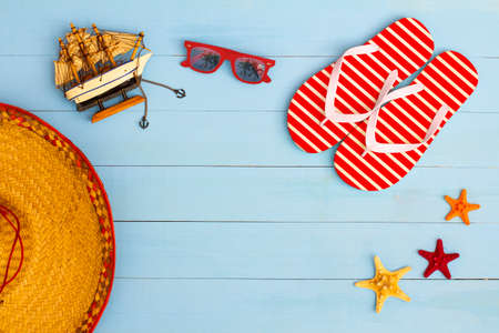 Summer time on a cool view on painted light blue wood table with sunglasses, flip flops, sailboat, hat and starfishの写真素材