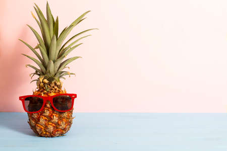 Summer concept about funny pineapple with sunglasses on blue wooden planks with pink background and copy space.の写真素材
