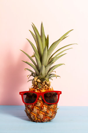 Summer concept about funny pineapple with sunglasses on blue wooden planks with pink background.の写真素材