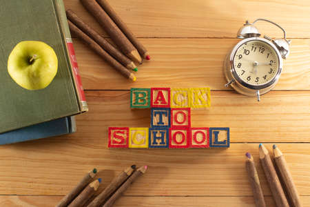 Spectacular representation of back to school with wooden cubes on a wooden table, books, green apple, old metal alarm clock and rustic colored crayons.の写真素材