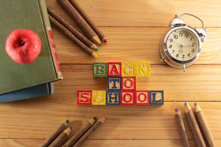 Spectacular representation of back to school with wooden cubes on a wooden table, books, red apple, old metal alarm clock and rustic colored crayons.の写真素材