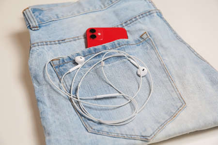 Red touch smartphone-phone with headphones in jeans pocket on white backgroundの写真素材