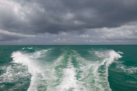 waves from the boat and cloudy sky on a horizontの写真素材