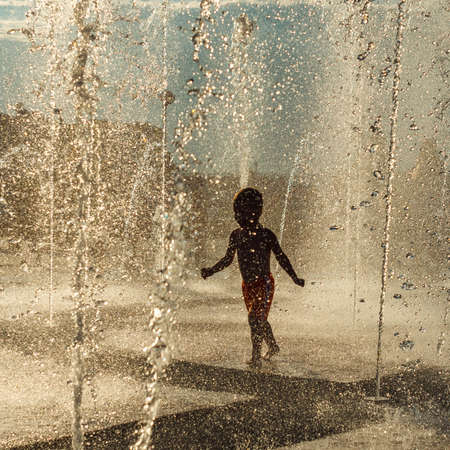 little boy running in the fountain splashing in backlightの写真素材