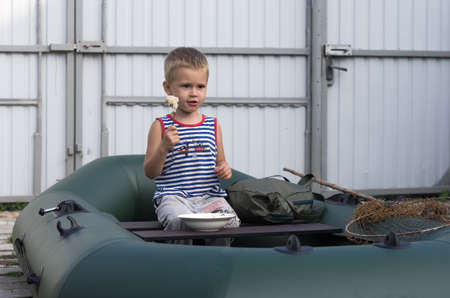 Boy 3 years old eating sausage in a boat in the yardの写真素材