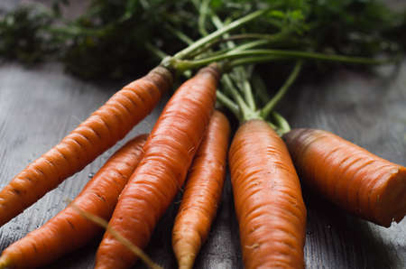 the orange carrots green foliage fresh harvest on a wooden surfaceの写真素材