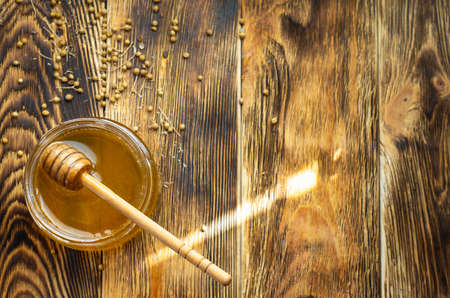 a honey jar on the bottom left on a wooden background with a spoonの写真素材