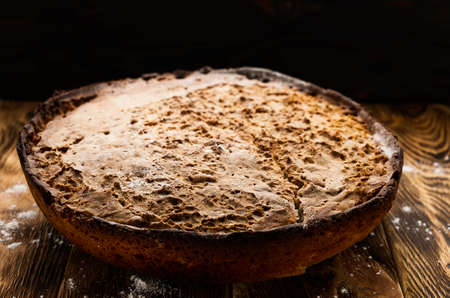 big whole handmade round black bread with interesting texture lie on dark wooden tableの写真素材