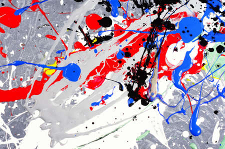 a spot of white and black and yellow and green and red and blue spilled paint on a concrete textured surface.の写真素材