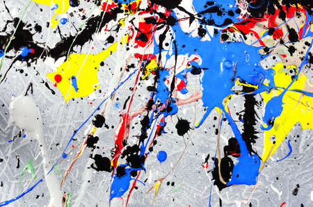 a spot of white and black and yellow and green and red and blue spilled paint on a concrete textured surface.の写真素材
