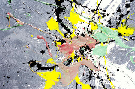 a spot of white and black and yellow and green and red spilled paint on a concrete textured surface.の写真素材