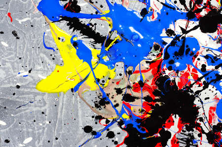 a spot of white and black and yellow and green and red and blue spilled paint on a concrete textured surface.の写真素材