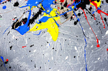 a spot of white and black and yellow and green and red and blue spilled paint on a concrete textured surface.の写真素材