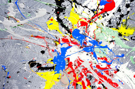 a spot of white and black and yellow and green and red and blue spilled paint on a concrete textured surface.の写真素材