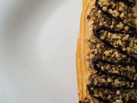 chocolate eclair sprinkled with nuts on a white plate.
