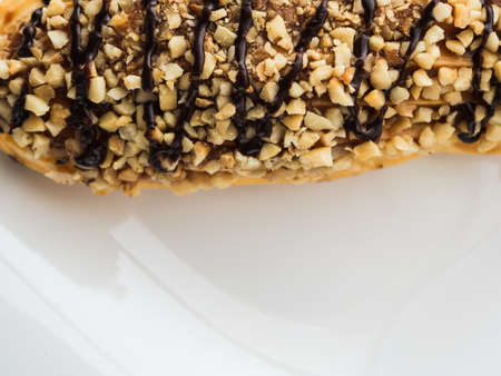 chocolate eclair sprinkled with nuts on a white plate.