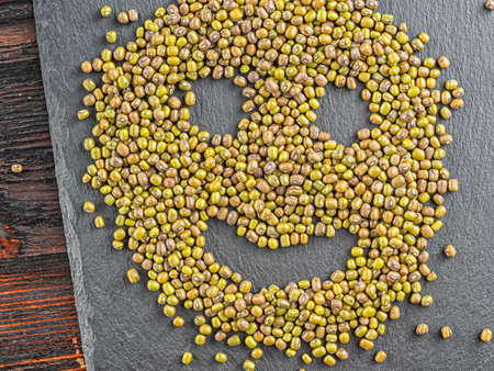 a smiling muzzle made from mung bean beans is on the surface of the slate. Green and brown grains...