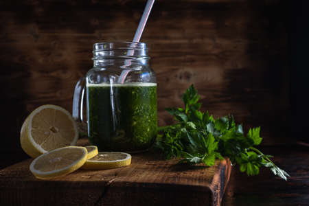 leafy celery and lemon smoothie. The smoothie poured into the Mason Jar next to it is cut pieces of lemon and celery leaves. All this lies on a thick wooden board. Wood background. horizontal orientation.の写真素材