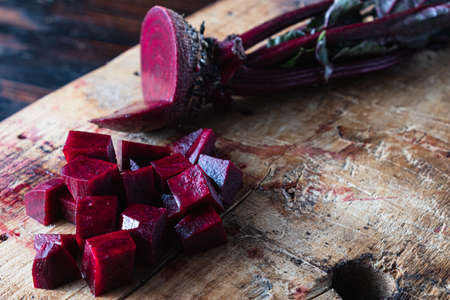 one juicy beets with leaves, one of which sliced lies next to diced beets on a wooden board. horizontal orientation. ugly food. dark background.の写真素材