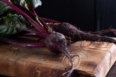 three unwashed juicy beets with green leaves lies on a wooden board. country style. rusty style....