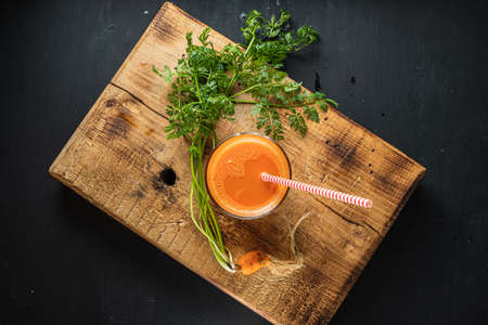 one litle ugly carrot. Glass with freshly squeezed carrot juice. one ugly carrot with green leaves. plastic free. cardboard tube. Wood background. horizontal orentecion. flat lay top viewの写真素材