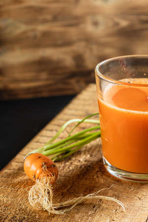 one litle ugly carrot. Glass with freshly squeezed carrot juice. one ugly carrot with green leaves. plastic free. cardboard tube. Wood background. vertical orentecion. close upの写真素材