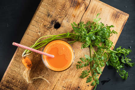 one litle ugly carrot. Glass with freshly squeezed carrot juice. one ugly carrot with green leaves. plastic free. cardboard tube. Wood background. horizontal orentecion. flat lay top viewの写真素材