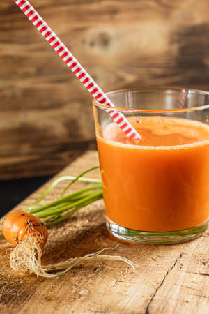 one litle ugly carrot. Glass with freshly squeezed carrot juice. one ugly carrot with green leaves. plastic free. cardboard tube. Wood background. vertical orentecion. close upの写真素材