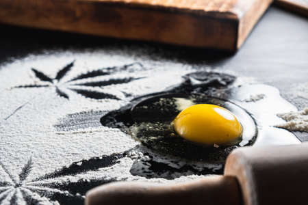 The process of making cannabis pastries. You can see a raw broken egg, a rolling pin, flour, and...