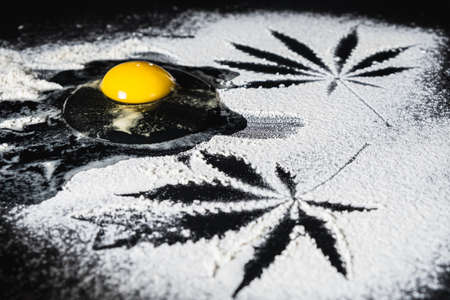 The process of making cannabis pastries. Traces of marijuana leaves on flour are visible, a broken raw eggの写真素材