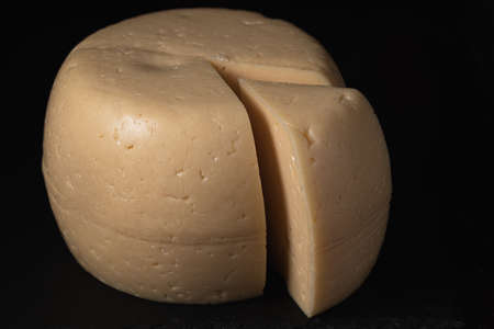 A cheese head and a sliced triangular slice lie on a slate dish. Horizontal orientation. Low-key...