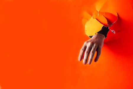 Children's hand protrudes through a torn gift in the surface of the color Lush Lava. Horizontal...