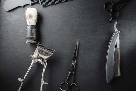 On a black dusty surface are old barber tools. Vintage manual hair clipper comb razor shaving brush...
