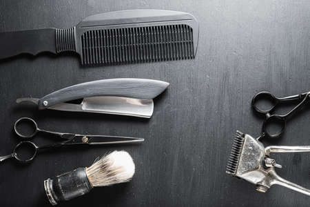 On a black dusty surface are old barber tools. Vintage manual hair clipper comb razor shaving brush shaving brush hairdressing scissors. horizontal top view flat layの写真素材