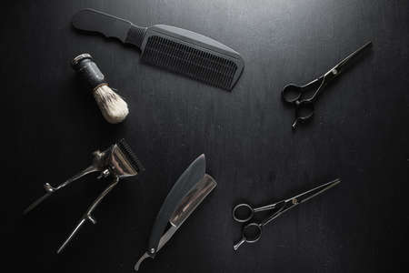On a black dusty surface are old barber tools. Vintage manual hair clipper comb razor shaving brush...