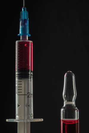 syringe and ampoule with red medicine on a dark background. Close-up. Vertical orientation
