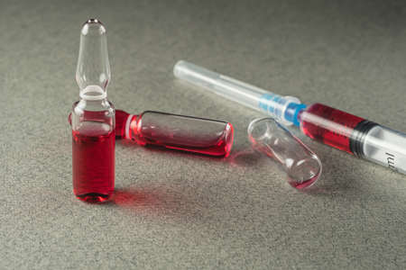 two full and one empty ampoule and syringe with red medicine on a gray background. Close-up. The full length of the medical needle. Horizontal orientationの写真素材