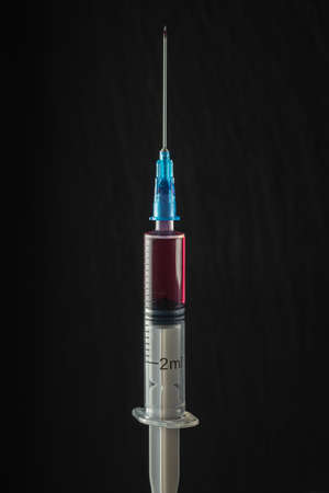 syringe with red medicine on a dark background. Close-up. Full length medical needle. Vertical orientationの写真素材