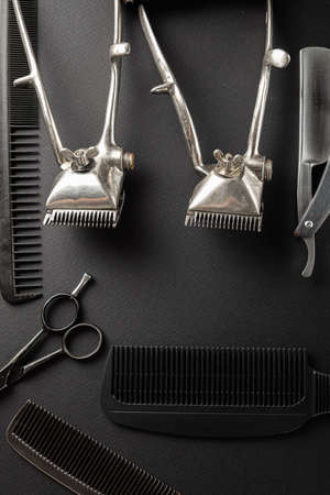 On a black surface are old hairdresser tools. Two vintage hand-held hair clippers, combs, razor,...