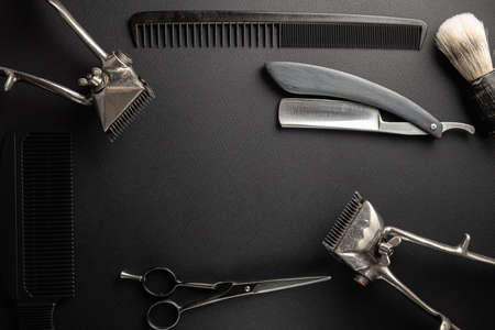 On a black surface are old hairdresser tools. Two vintage hand-held hair clippers, combs, razor,...