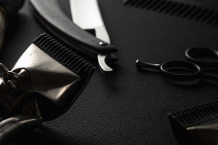 On a black surface are old barber tools. Two vintage manual hair clipper, razor, shaving brush,...