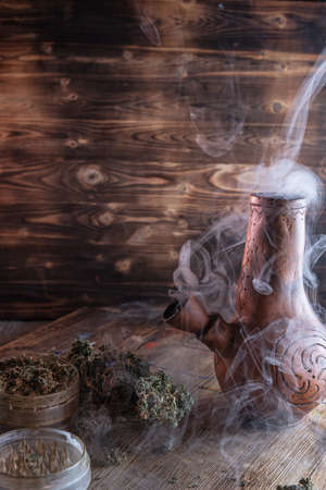 steaming bong. open grinder with marijuana. cannabis on a wooden surface. on a wooden tray stained...