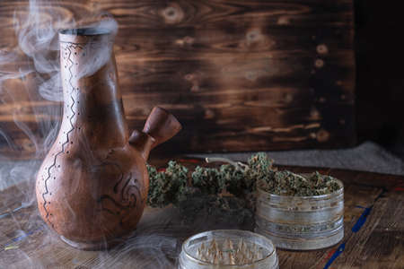 smoke bong. open grinder with marijuana. cannabis on a wooden surface. on a wooden tray stained with...