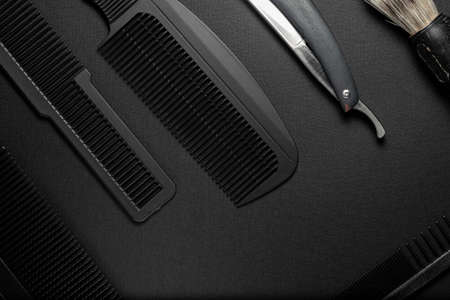 On a black surface are old hairdresser tools. combs, razor, shaving brush. black monochrome....