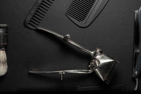 On a black surface are old hairdresser tools. vintage hand-held hair clipper, hairdressing scissors, combs, razor, shaving brush. black monochrome. horizontal orientation. top view flat leyの写真素材