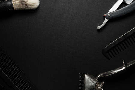 On a black surface are old hairdresser tools. vintage hand-held hair clipper, hairdressing scissors, combs, razor, shaving brush. black monochrome. horizontal orientation. top view flat ley. copy spaceの写真素材
