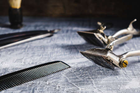 On a painted concrete surface are old hairdresser tools. two vintage hand-held hair clipper,...