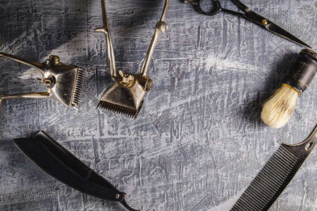 On a painted concrete surface are old hairdresser tools. two vintage hand-held hair clipper, hairdressing scissors, combs, razor, shaving brush. horizontal orientation. top view flatleyの写真素材