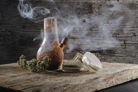 bong with marijuana smokes. Nearby is a bud of medical cannabis and a grinder. old wood background....