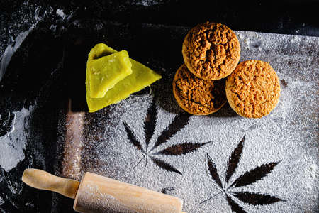 traces of marijuana leaves on flour, and rolling pin and three cookies and cannabis butter. on a rusty pan. top view flat lay. Horizontalの写真素材